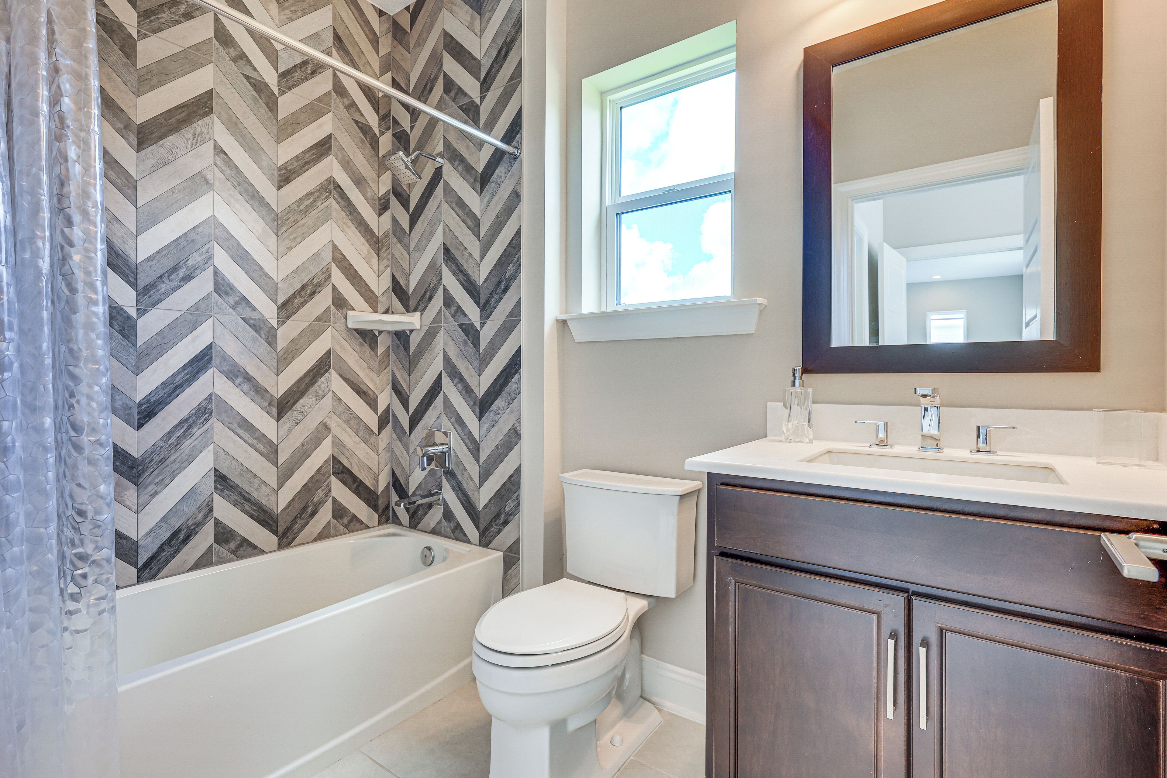 A modern bathroom with a herringbone tile backsplash, a white bathtub, a toilet, and a vanity with a mirror.