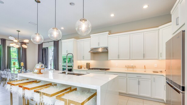 A modern kitchen with white cabinetry, a central island with bar stools, pendant lighting, and a stainless steel refrigerator.