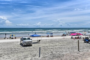 Una playa con una camioneta blanca estacionada en la arena, sombrillas y una vista despejada del océano.