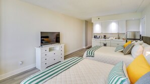 Une chambre avec deux lits, une télévision, une commode et un coin cuisine.