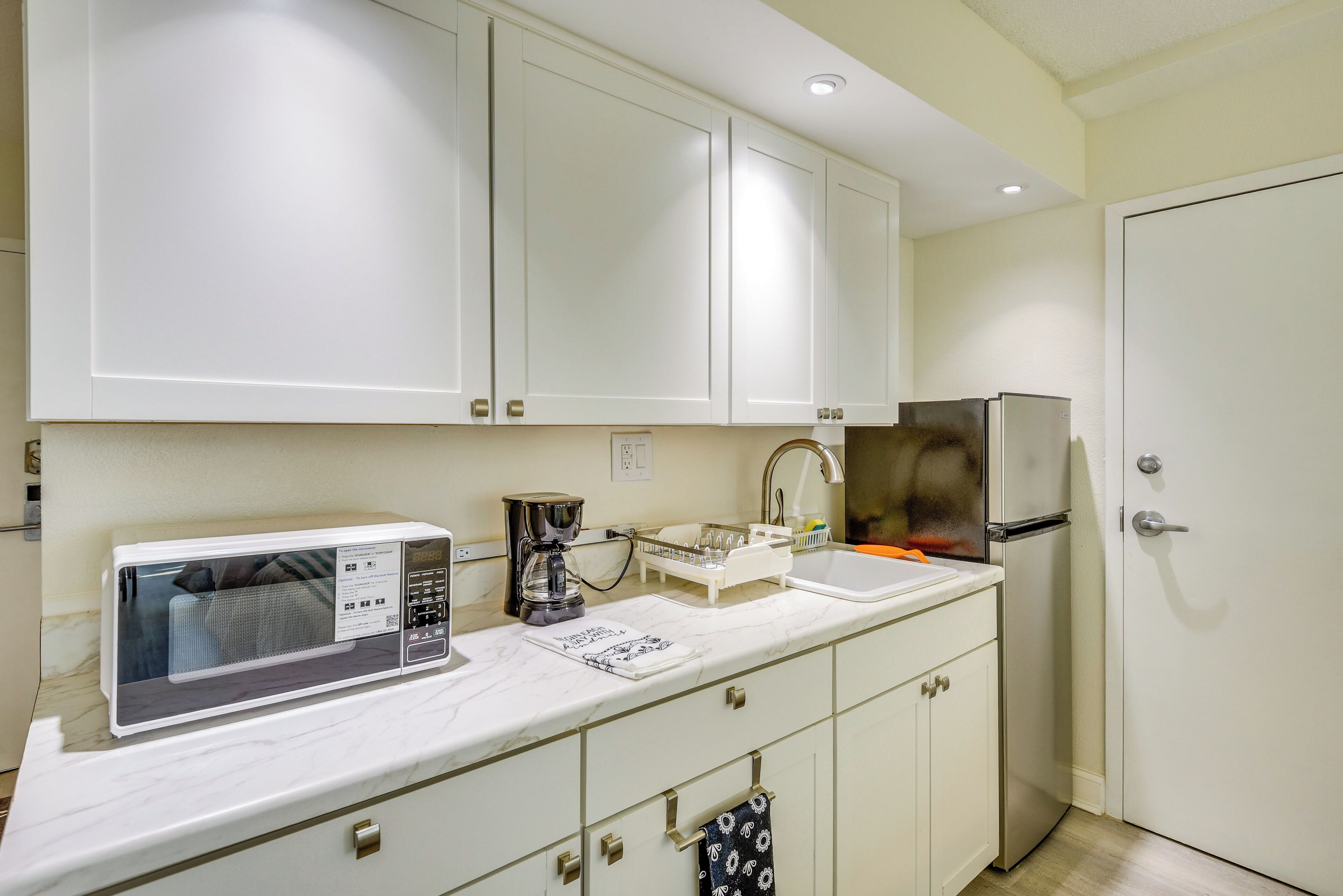 A kitchen with white cabinets, a microwave, a coffee maker, and a refrigerator.