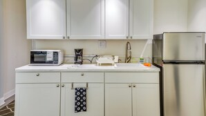Une cuisine avec des meubles blancs, un réfrigérateur en acier inoxydable, un four à micro-ondes et une machine à café.