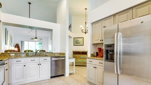A spacious kitchen with white cabinets, a stainless steel refrigerator, and a granite countertop. - 5 Mi to Naples Beach - Getaway w/ Screened Lanai! (Naples)