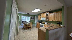 Una cocina con armarios de madera, microondas, estufa y comedor con sillas y mesa.