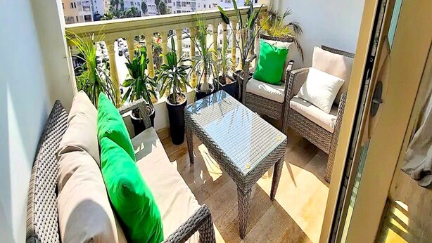 A balcony with wicker furniture, green cushions, and potted plants. - Casa Sahifa (Casablanca)