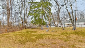 A grassy yard with trees and a house in the background. - Modern Home w/ Spacious Yard in Springfield! (Springfield)