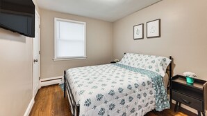 A bedroom with a bed, a nightstand, a window with blinds, and two framed pictures on the wall. - Modern Home w/ Spacious Yard in Springfield! (Springfield)