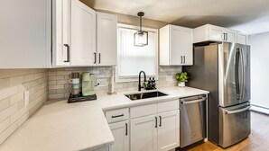 A modern kitchen with white cabinets, a stainless steel refrigerator, a coffee maker, and a window with blinds. - Modern Home w/ Spacious Yard in Springfield! (Springfield)