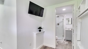 A hallway with a mounted TV, a small plant on a white shelf, and a view into a bathroom with a shower and toilet. - 1 Mi to Dtwn: Renovated Retreat in Georgetown! (Georgetown)