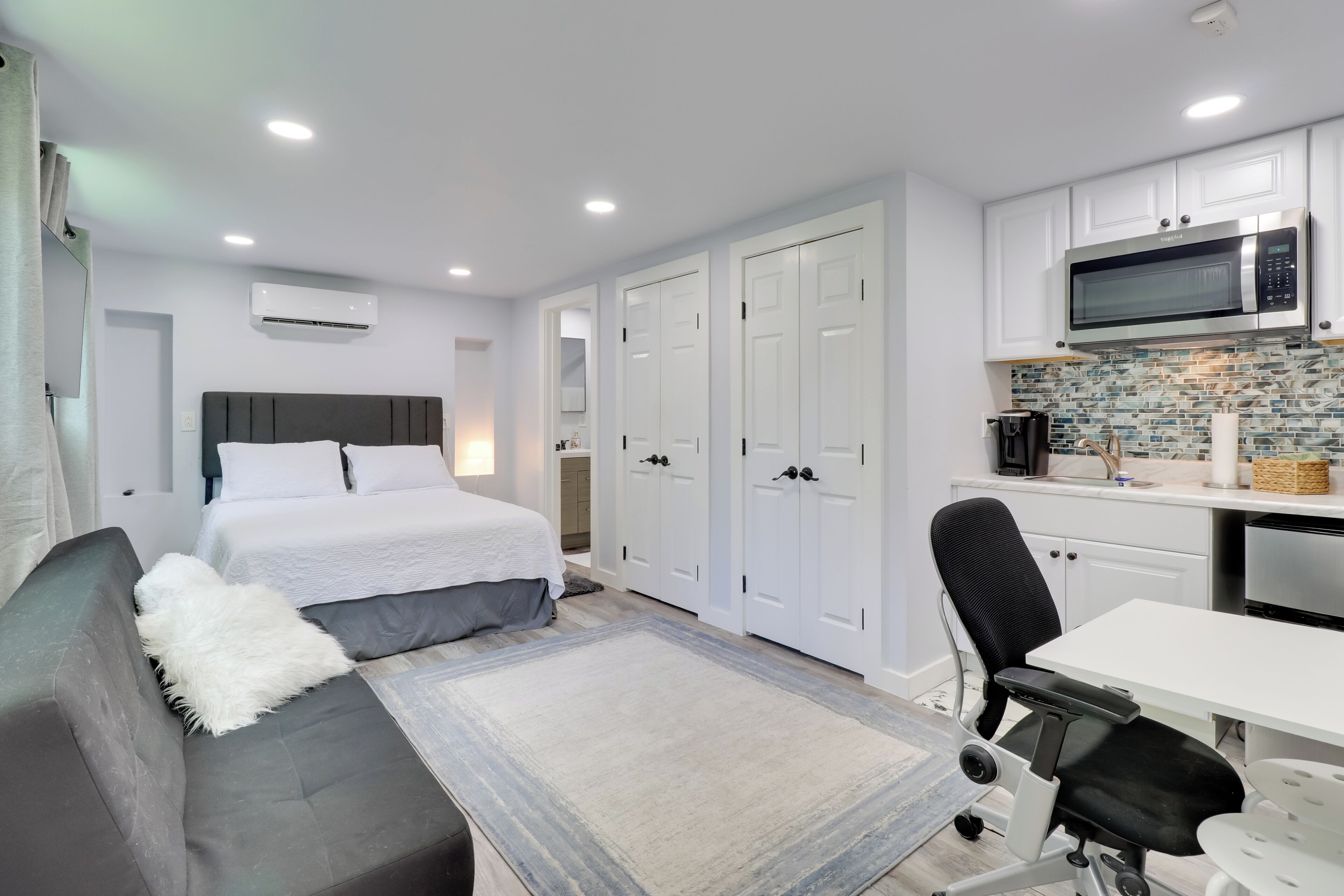 A compact room with a bed, a sofa, a desk, and a kitchenette.