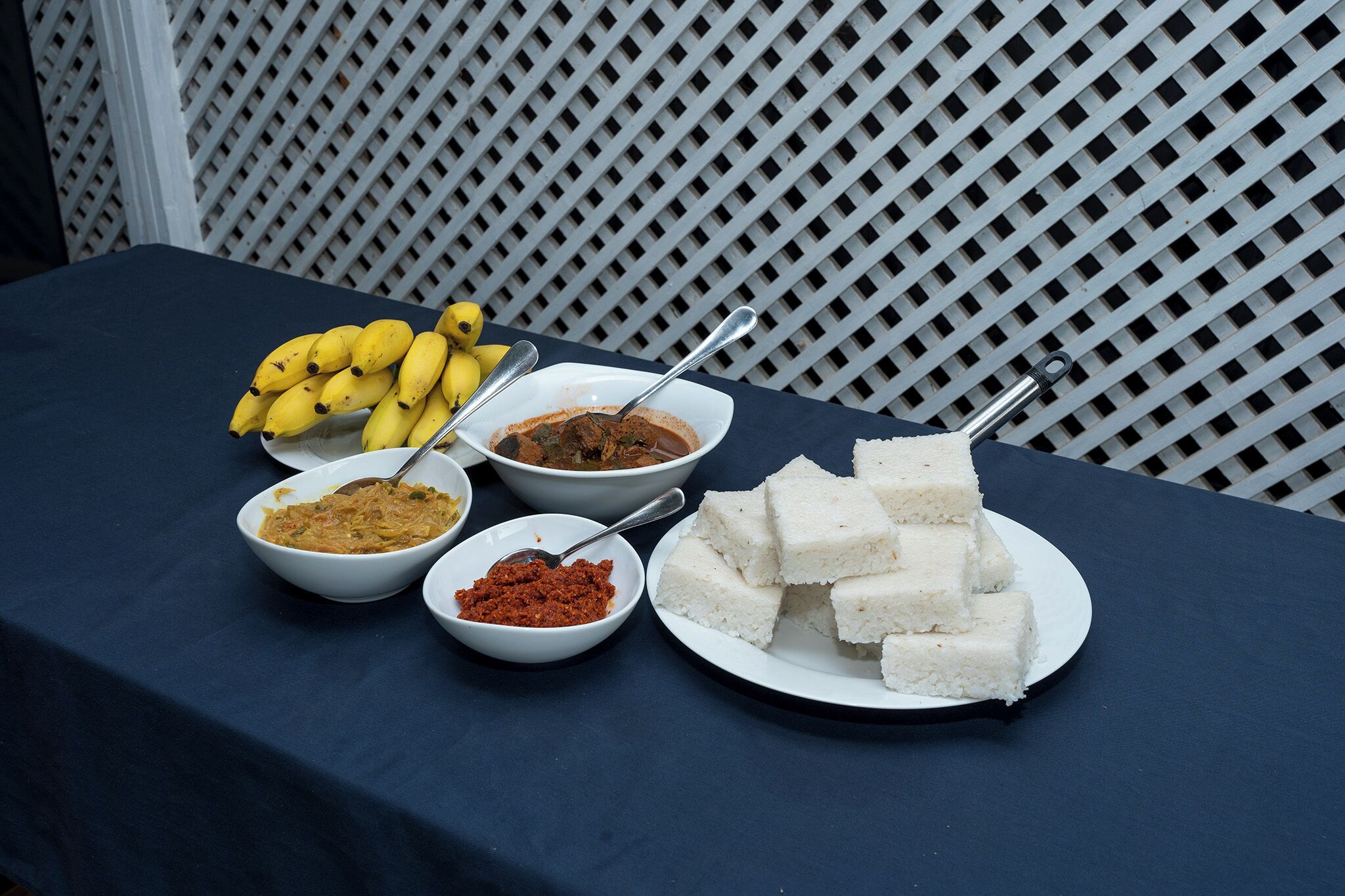 Una mesa con diferentes alimentos, incluyendo plátanos, recipientes con distintas salsas y cubos de arroz blanco.
