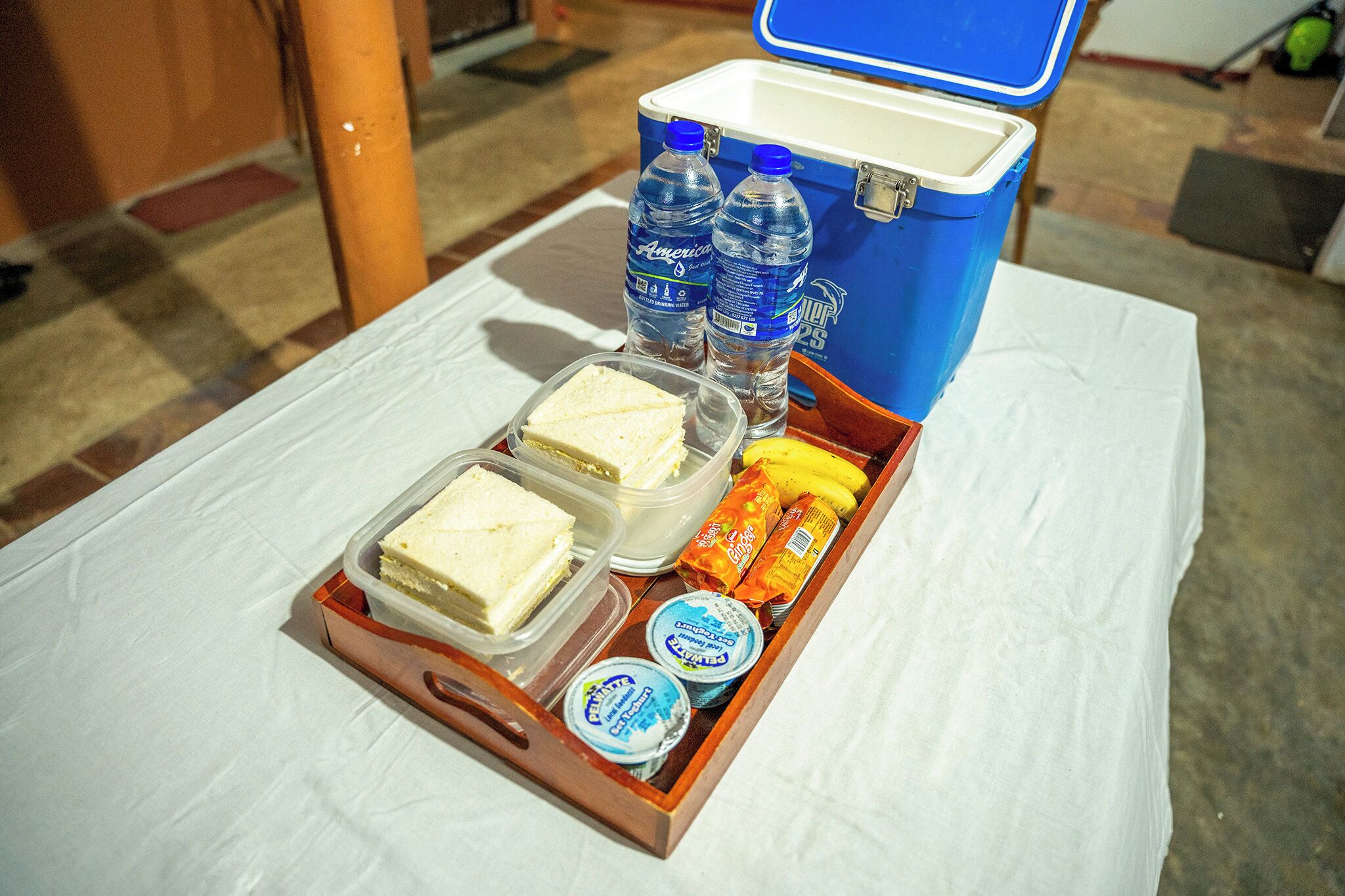 Ein Tablett mit Sandwiches, Wasserflaschen, einer Banane und Joghurtbechern auf einem Tisch.