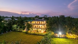 A large, multi-story building with a balcony, surrounded by lush greenery and palm trees. - Mailagama Cinnamon Residence (Sella Katharagama)