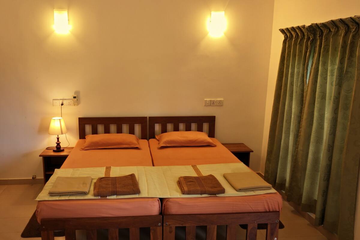 A double bed with two pillows, a bedside table with a lamp, and a power outlet on the wall.