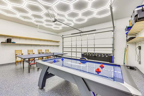 A room with a foosball table, a ping pong table, and a hexagonal ceiling light fixture.