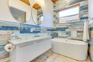A bathroom with a large bathtub, two sinks, and a window.