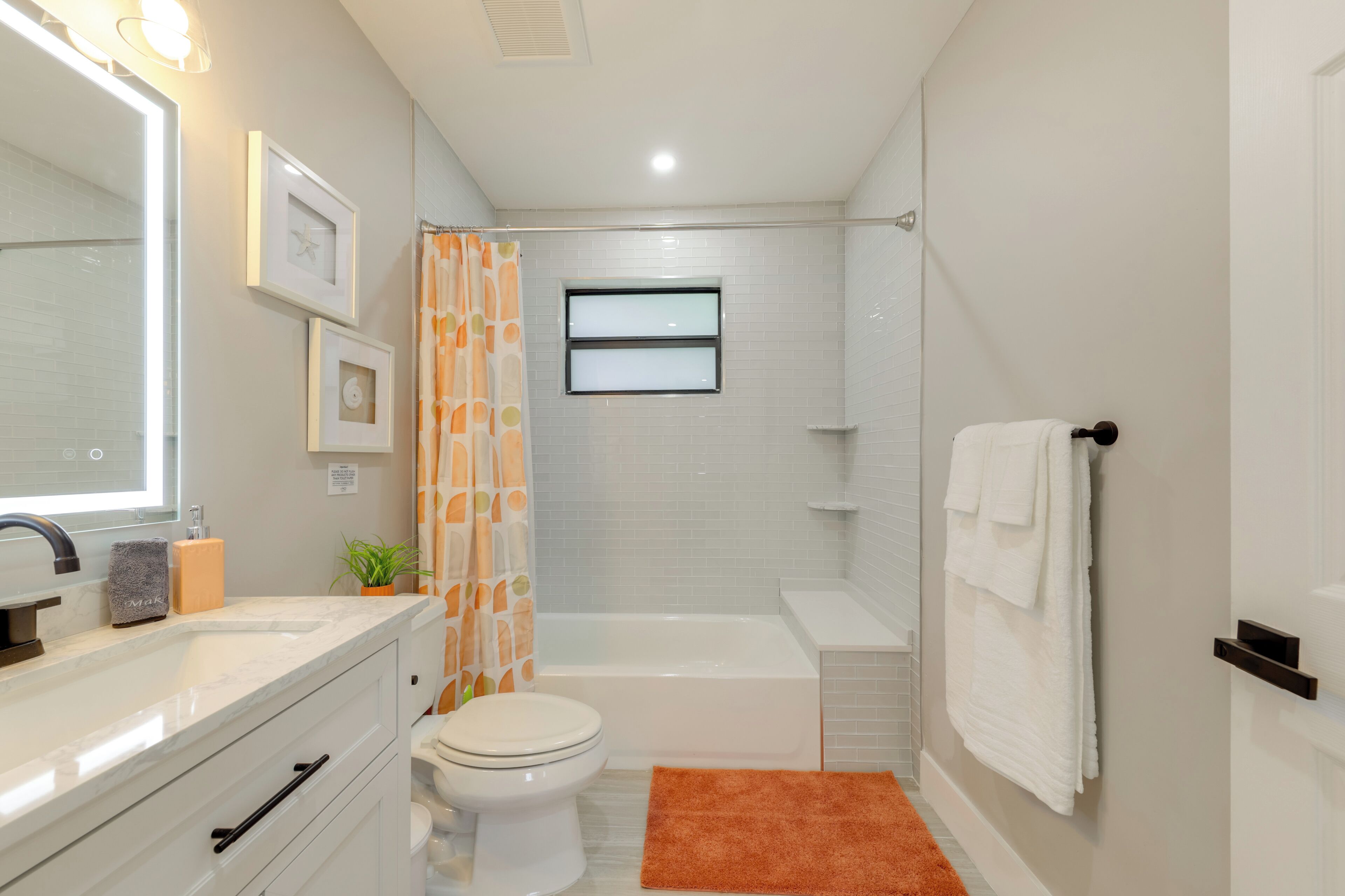 Ein modernes Badezimmer mit Waschbecken, Toilette und Badewanne in Weiß. Ein Duschvorhang, ein Handtuchhalter und ein kleines Fenster über der Badewanne sind vorhanden.