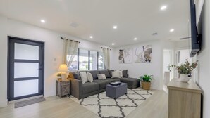 A modern living room with a sectional sofa, a coffee table, and a TV mounted on the wall. - Private Yard! Getaway 3 Mi to Hard Rock Stadium (Miramar)