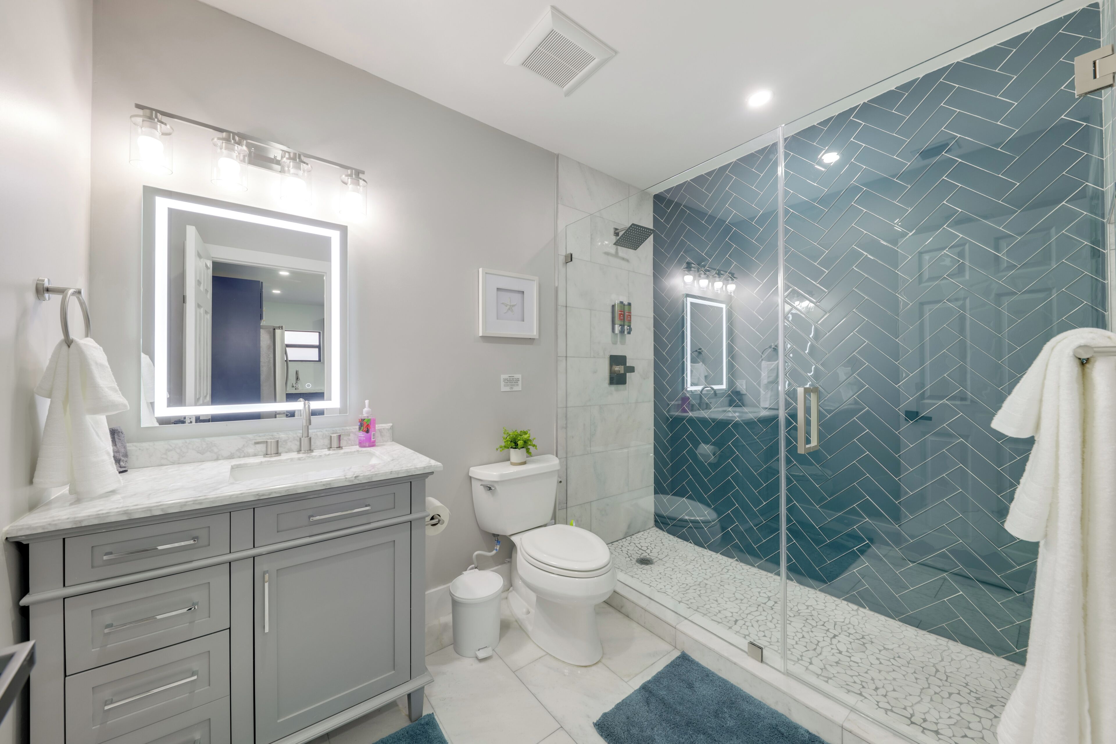 A modern bathroom with a glass-enclosed shower, a white toilet, and a vanity with a mirror and lights.