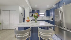 A modern kitchen with a marble island, two bar stools, a stainless steel refrigerator, and blue cabinets. - Private Yard! Getaway 3 Mi to Hard Rock Stadium (Miramar)