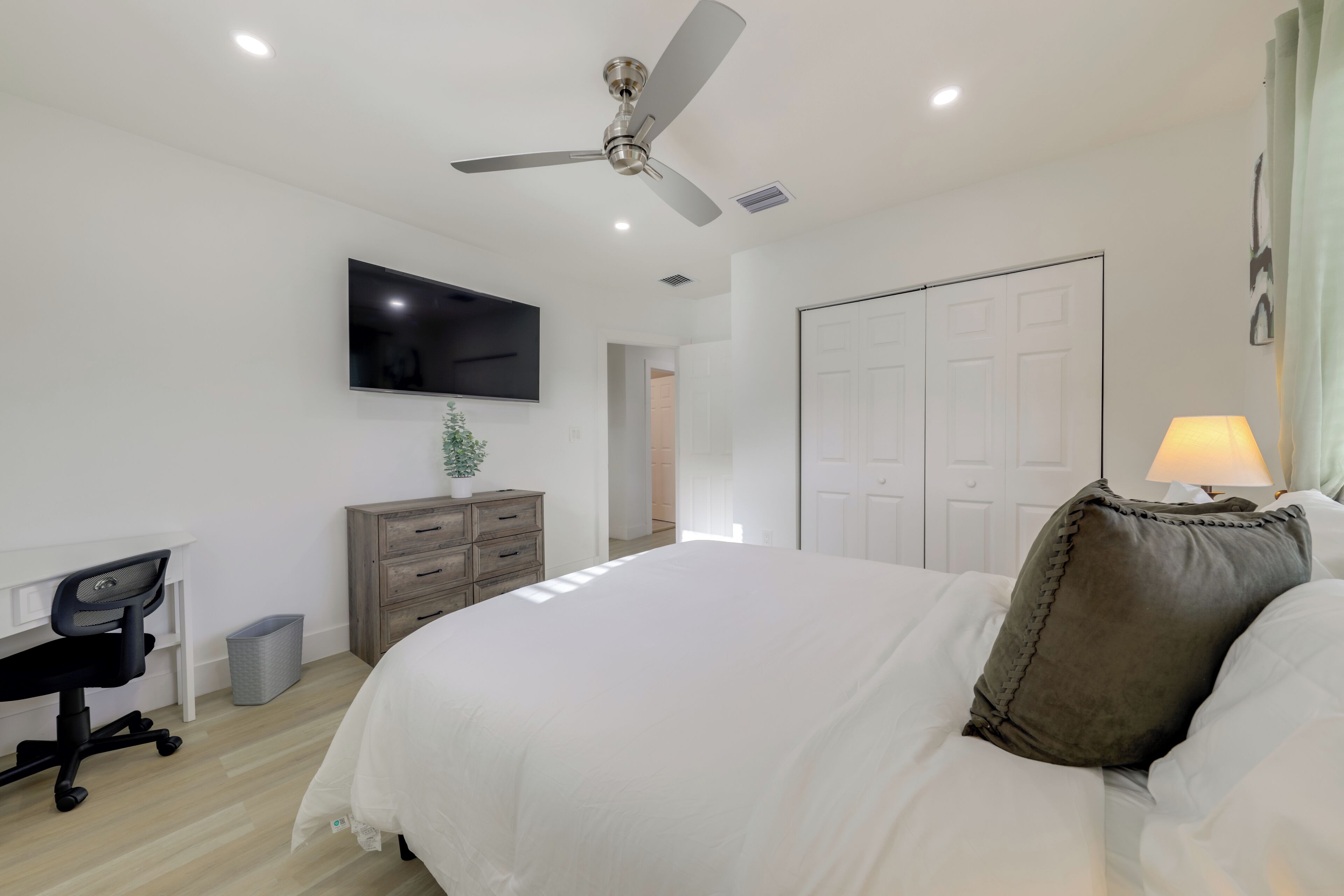 A bedroom with a bed, a desk, a chair, a TV, a ceiling fan, and a wardrobe.