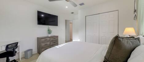 A bedroom with a bed, a desk, a chair, a TV, a ceiling fan, and a wardrobe.