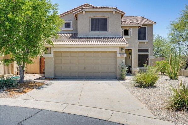 A two-story house with a garage, a tree in the driveway, and desert landscaping.