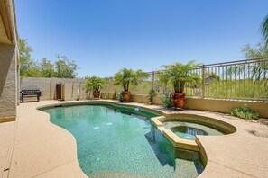A swimming pool with a curved design, surrounded by a fence and potted plants.