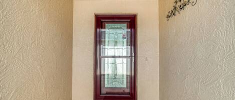 A door with a glass panel and a red frame, a welcome mat, and a textured wall with a decorative metal piece.