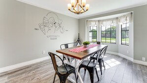 A dining room with a wooden table, black chairs, a chandelier, and a wall mural. - Disney-themed Home: Swim, BBQ & Explore Kissimmee! (Kissimmee)