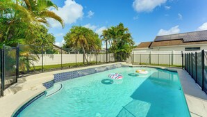 A swimming pool with clear blue water, surrounded by a fence and palm trees. - Disney-themed Home: Swim, BBQ & Explore Kissimmee! (Kissimmee)