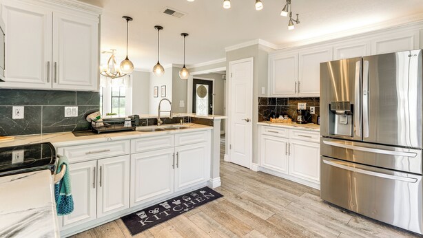 A modern kitchen with white cabinets, a stainless steel refrigerator, pendant lights, and a marble backsplash. - Disney-themed Home: Swim, BBQ & Explore Kissimmee! (Kissimmee)