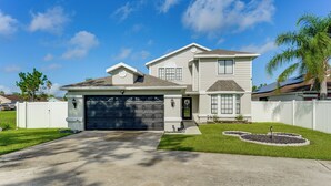 A two-story house with a garage, a well-maintained lawn, and a small garden area. - Disney-themed Home: Swim, BBQ & Explore Kissimmee! (Kissimmee)