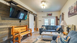 A living room with a wooden bench, a sofa, a coffee table, and a TV mounted on the wall. - Hot Tub + Pet Friendly: Quiet French Creek Getaway (French Creek)
