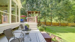 A covered patio with outdoor furniture, a wooden deck, and a view of a well-maintained lawn and trees.