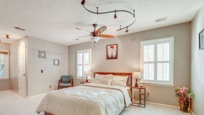 A bedroom with a bed, a ceiling fan, a window with blinds, a chair, and a vase with flowers.