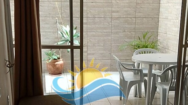 Una habitación con cama, ventana con cortinas, suelo de baldosas, mesa con sillas y plantas en macetas.