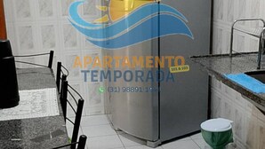 Una cocina con un refrigerador de acero inoxidable, una mesa de comedor con sillas, un lavamanos y un inodoro.