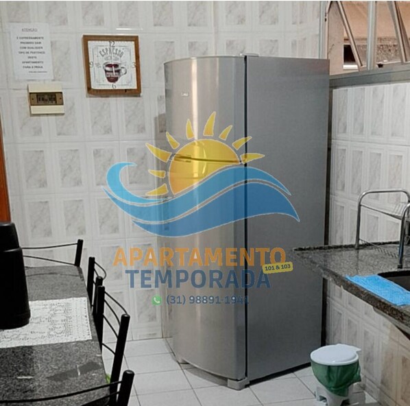 Una cocina con un refrigerador de acero inoxidable, una mesa de comedor con sillas, un lavamanos y un inodoro.
