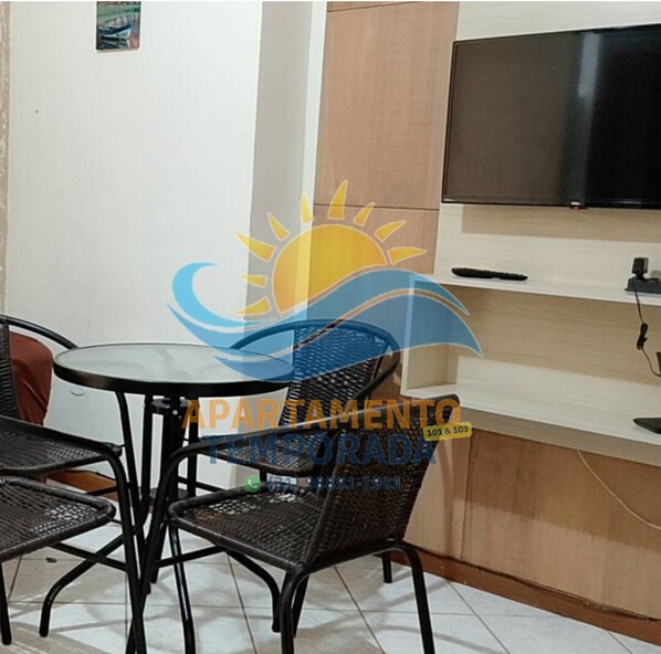 A small room with a TV mounted on the wall, a table with chairs, and a cabinet below the TV.