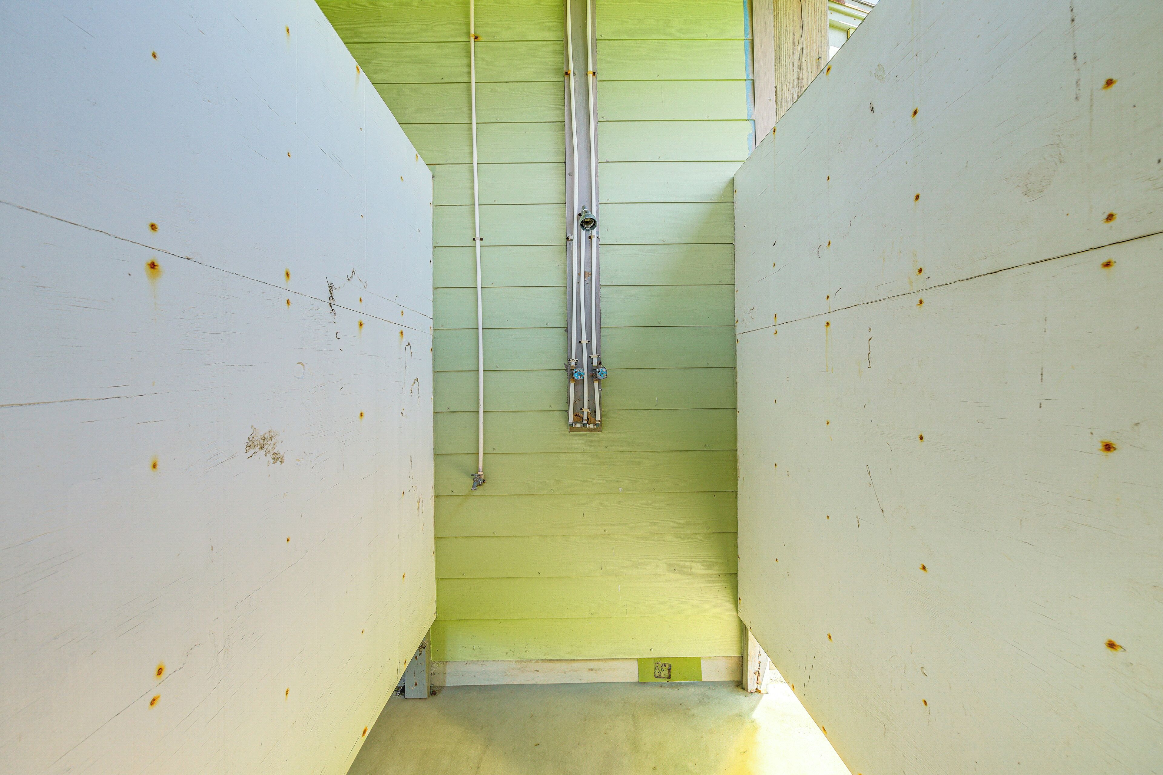 Un pasillo estrecho con paredes verdes y techos blancos, que presenta una tubería vertical en el centro y una pequeña ventana.