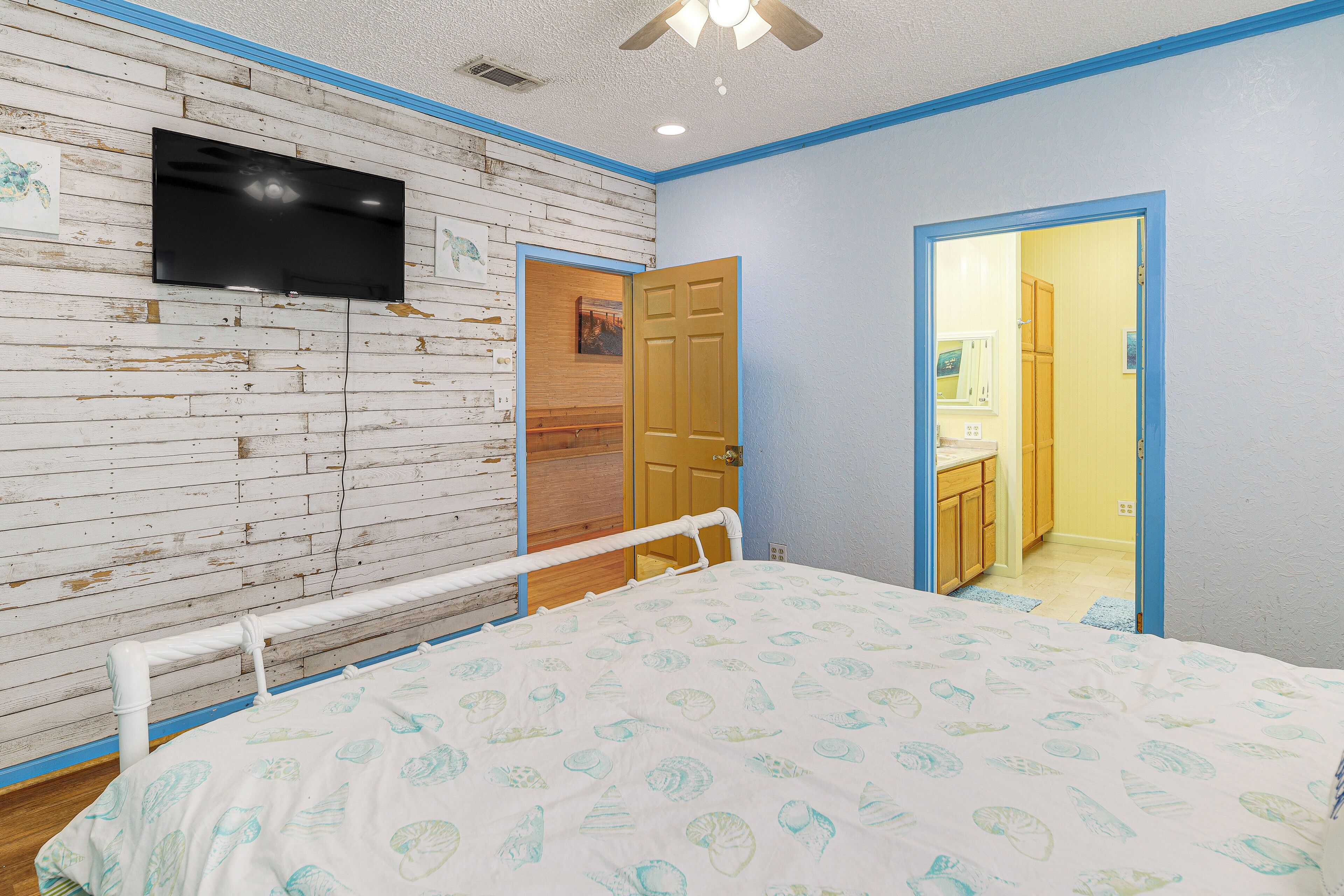 Een slaapkamer met een houten wand, een flatscreen televisie, een bed met een bedovertrek met dessin en een deur naar een badkamer.