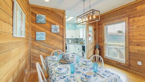 A wooden interior with a dining table set for four, white chairs, and a kitchen visible through an open door. - Walk to Beach: Getaway on Bolivar Peninsula! (Port Bolivar)