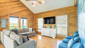 A cozy living room with a wooden ceiling, a gray sofa, a white dresser, and a blue chair. - Walk to Beach: Getaway on Bolivar Peninsula! (Port Bolivar)