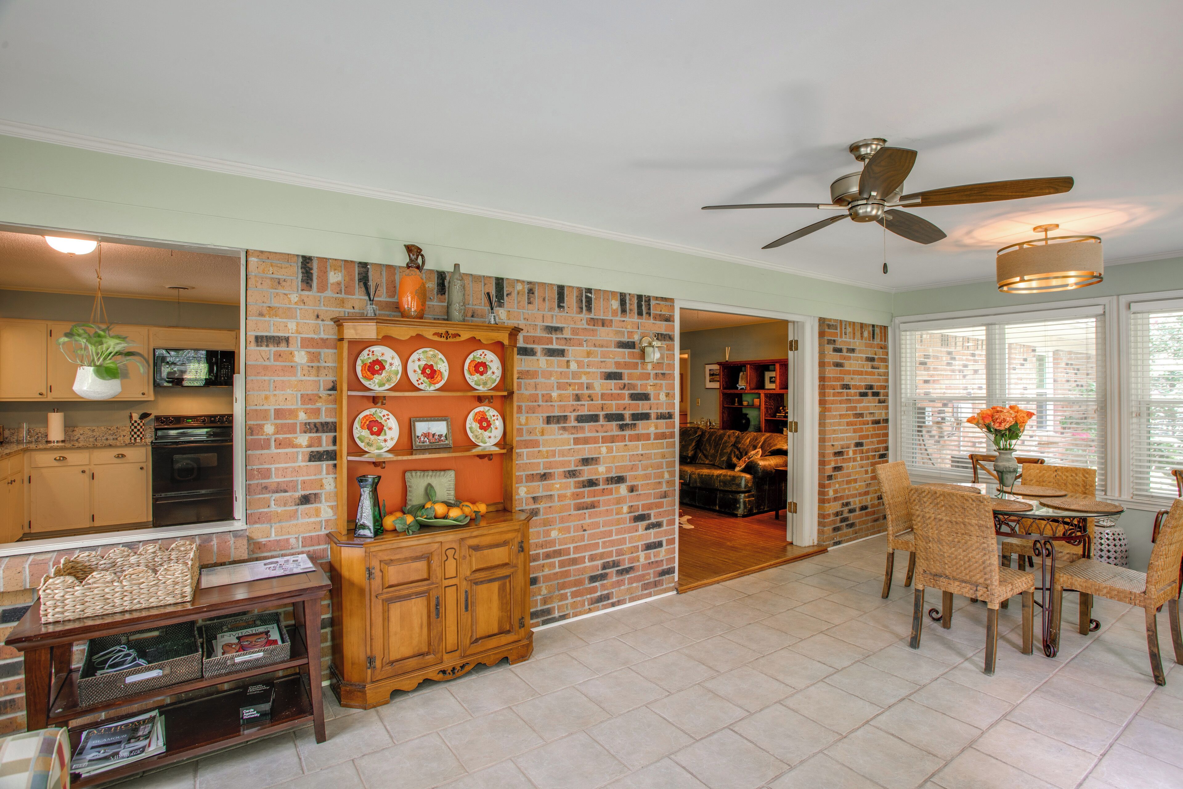 A spacious living area with a brick wall, a dining table with chairs, and a ceiling fan.