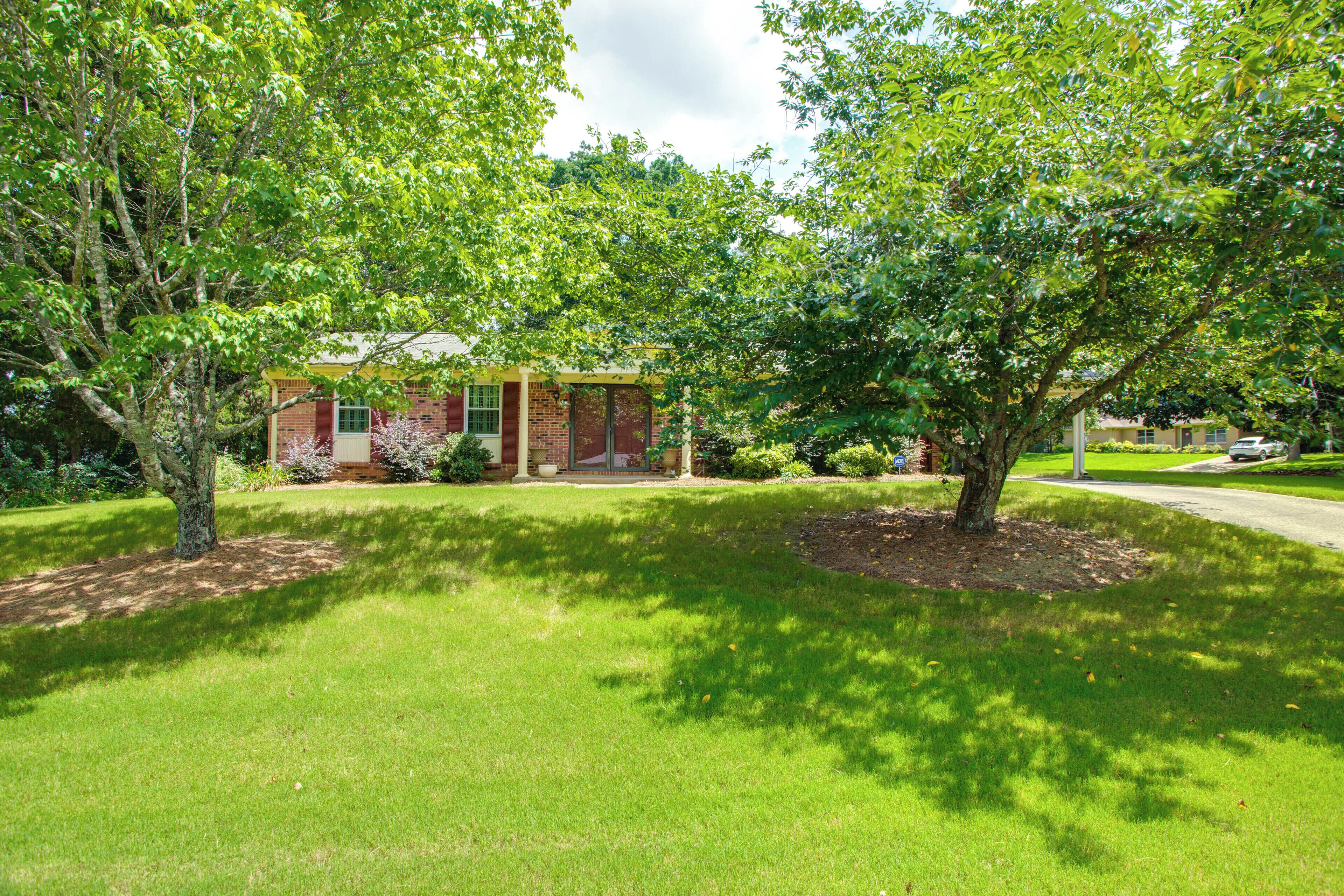 A residential house with a brick exterior, surrounded by a well-maintained lawn and large trees.