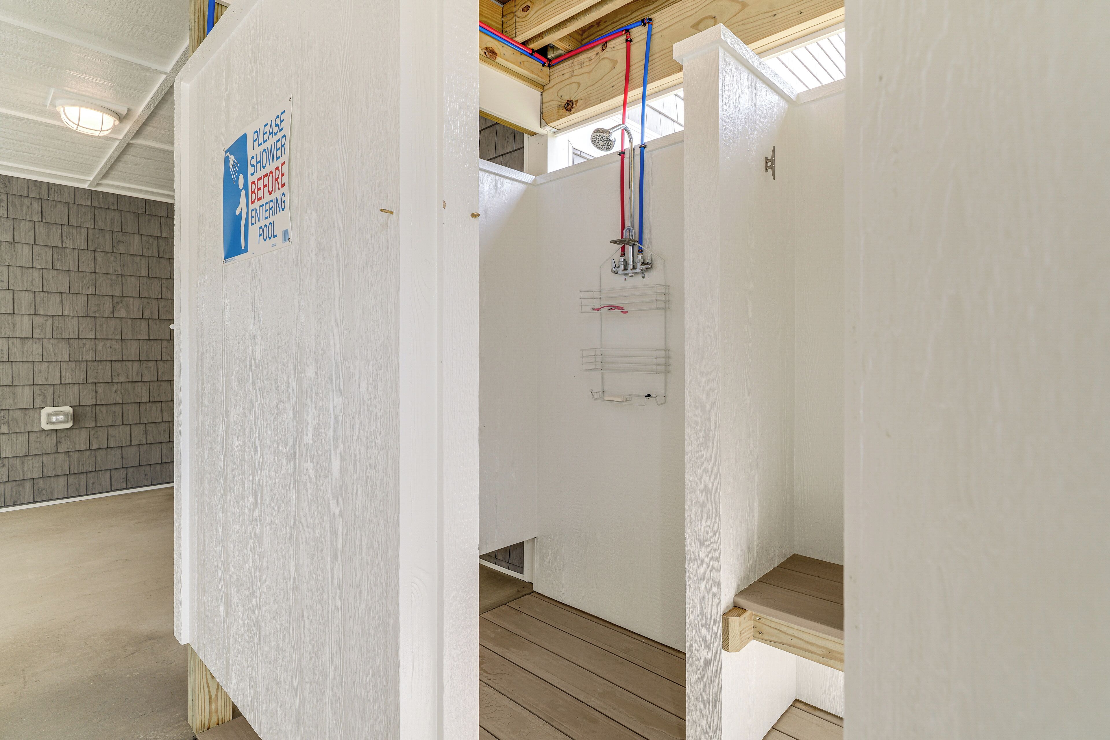 A shower area with a sign instructing to shower before entering the pool.