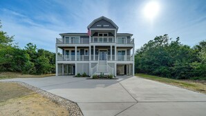 A two-story building with a balcony, a flag, and a clear sky. - Walk to Beach: Southern Shores Retreat w/ Hot Tub (Kitty Hawk)