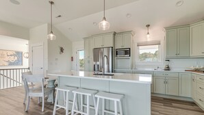 A modern kitchen with a large island, bar stools, stainless steel appliances, and light green cabinetry. - Walk to Beach: Southern Shores Retreat w/ Hot Tub (Kitty Hawk)