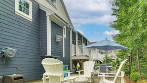 Une terrasse avec des fauteuils Adirondack blancs, une table et un parasol bleu.